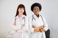 Two smiling happy African and Caucasian female doctors colleagues, wearing white coats, standing side by side with Royalty Free Stock Photo