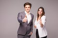 Two smiling happy business people in formalwear showing thumbs-up on gray background Royalty Free Stock Photo