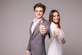 Two smiling happy business people in formalwear showing thumbs-up on gray background Royalty Free Stock Photo