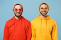 Two smiling hipster men guys in fashion red yellow clothes eyeglasses posing isolated on pastel blue background studio Royalty Free Stock Photo