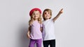 Two smiling kids girl and boy in stylish clothing stand together hugging each other and pointing at something above