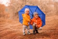 Two smiling little toddlers, brother and sister, hiding together under big blue umbrella in autumn park Royalty Free Stock Photo