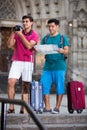 Two smiling male tourists are walking with map and photographing