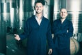 Two smiling men in uniforms standing in winery fermentation comp