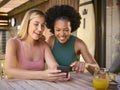 Two Smiling Multi-Cultural Female Friends Outdoors At Home Looking At Mobile Phone Royalty Free Stock Photo