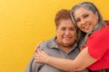 Two smiling older adult Mexican women against yellow background