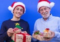 Two smiling people, a white-haired grandfather with the awesome teenager grandson, offering Christmas gifts with red ribbon.