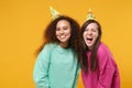 Two smiling screaming women friends european and african american girls in pink green clothes, birthday hats posing