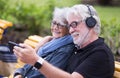 Two smiling  senior people white haired sitting on a yellow bench looking at the same smart phone, bearded man with headphones, Royalty Free Stock Photo