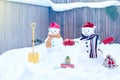 Two smiling snowman - happy couple  in knitted mittens, scarf and red caps with gifts and shovel  in the back yard Royalty Free Stock Photo