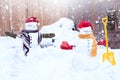 Two smiling snowmen - happy couple  in knitted mittens, scarf and red caps with gifts and shovel  in snowfall Royalty Free Stock Photo