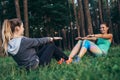 Two smiling sportswomen training outdoors doing full sit-ups sitting opposite each other on grass in forest