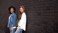 Two smiling university students leaning brick wall, leisure time college campus