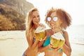 Two women in bikinis drinking from coconuts on a beach Royalty Free Stock Photo