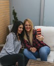 Two smiling young girls drinking beers and taking selfies with a mobile on a terrace