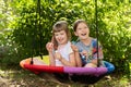 Two smiling young girls enjoy a sunny day outdoors, blowing soap bubbles while seated on a colorful garden swing outside. Summer Royalty Free Stock Photo