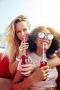 Two smiling young women sitting on a boat sipping drinks