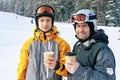 Two snowboarders of different ages are drinking hot coffee. Ski slope background. Father and son Caucasian ethnicity Royalty Free Stock Photo