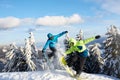 Two snowboarders doing tricks at ski resort. Riders friends performing jump with their snowboards near forest on