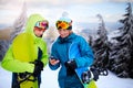 Two snowboarders talking and holding smartphones. Friends looking at cellphone and communicating in social network Royalty Free Stock Photo