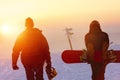 Two snowboarders walking against sunset sky