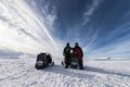 Two snowmobiles back side and two friends pose around of one snowmobile. They dressed for driving in cold mountains