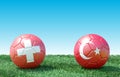 Two soccer balls in flags colors on green grass. Switzerland and Turkey.