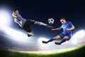 Two soccer players in mid air kicking the soccer ball, stadium lights at night in background Royalty Free Stock Photo