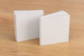 Two softcover or paperback square white mockup books standing on the wooden background. Blank front and back cover