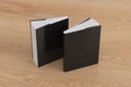 Two softcover or paperback vertical black mockup books standing on the wooden background. Blank front and back cover