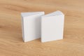 Two softcover or paperback vertical white mockup books standing on the wooden background. Blank front and back cover