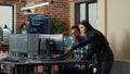 Two software developers holding laptop with coding interface walking towards desk and sitting down Royalty Free Stock Photo