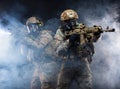 Two soldiers in military gear, bulletproof vests and gas masks cover each other and raise their submachine guns taking