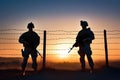 Two soldiers standing guard at a barbed wire fence at sunset, keeping watch over the perimeter Royalty Free Stock Photo