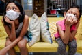 Two Asian Little Girls Wearing Medical Face Mask Getting Bored Sitting on Sofa Apart from Each Other