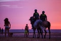 Two spanish police officers patrolling beach at sunset on horseback