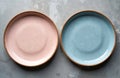 Two speckled ceramic plates, one pink and one blue, are shown side by side on grey textured surface. They are empty and ready for Royalty Free Stock Photo