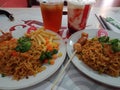 two spicy chili noodles served on a round plate containing sausages and potatoes plus two fresh drinks