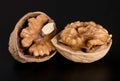 Two split beautiful textured walnuts in a shell on a glossy black background Royalty Free Stock Photo