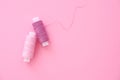 Two spools of sewing thread lilac pink, violet, crimson on a pink paper backgroun Royalty Free Stock Photo