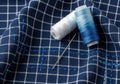Two spools of thread and a needle rest on a dark blue checkered fabric isolated on white background Royalty Free Stock Photo