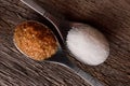 Two spoons with brown cane sugar and white sugar next to each other on wooden board.