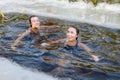 two sporting beautiful young women swimming in an ice hole in a winter sunny day