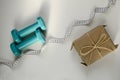 Two sports dumbbells, gift box and white measuring tape on white background with copy space. Christmas sport flatlay. Home