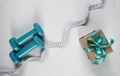 Two sports dumbbells, gift box and white measuring tape on white background with copy space. Christmas sport flatlay. Home