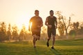 The two sportsmen running on the grass on the sunset background.