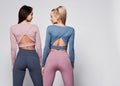 Two sporty blonde and brunette girls in athletic body cloth sport wear cloth stand together after workout on gray Royalty Free Stock Photo