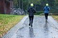 Two sporty female people from behind with neon yellow caps jogging in the rain through an autumn park, there is no bad weather for Royalty Free Stock Photo