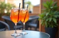 Two Spritz cocktails sit on a dark table outdoors. The drinks are served with ice cubes and straws in a modern bar setting. This Royalty Free Stock Photo