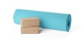 Two stacked yoga or pilates blocks made from natural cork with blue, rolled yoga or pilates mat over white background